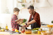 © deniskomarov - Son reading cookbook to dad cooking dinner at modern bright loft kitchen.