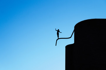 monument to silhouette of a boy balancing on tube like tightrope walking against background of a blu