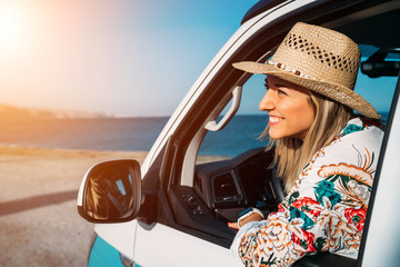 Portrait of an attractive smiling woman with straw hat driving her car near the beach in summer - Close-up