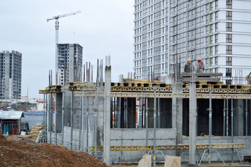 Working male builders are working on the roof of a large monolithic frame house, building, and new building under construction. Construction of the building in the new micro district of the big city