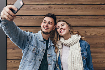 Inspired man with beard making selfie with his girlfriend. Gorgeous young woman with black scarf posing on wooden background.