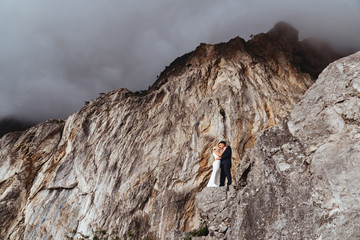 Wall Mural - Young newly wed couple, bride and groom kissing, hugging on perfect view of mountains, wedding concept