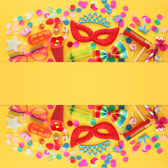 Wall Mural - Party colorful noisemaker, mask and cute clown doll over yellow wooden background . Top view, flat lay