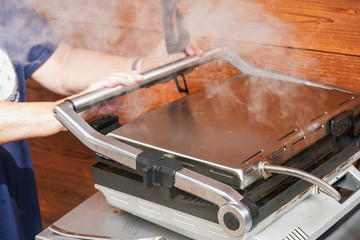 Detail on woman hands holding closed electric grill handle, smoke above as food is grilled