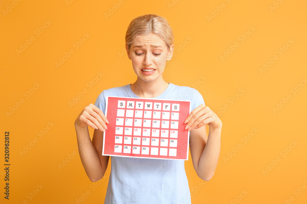 Young woman with menstrual calendar on color background