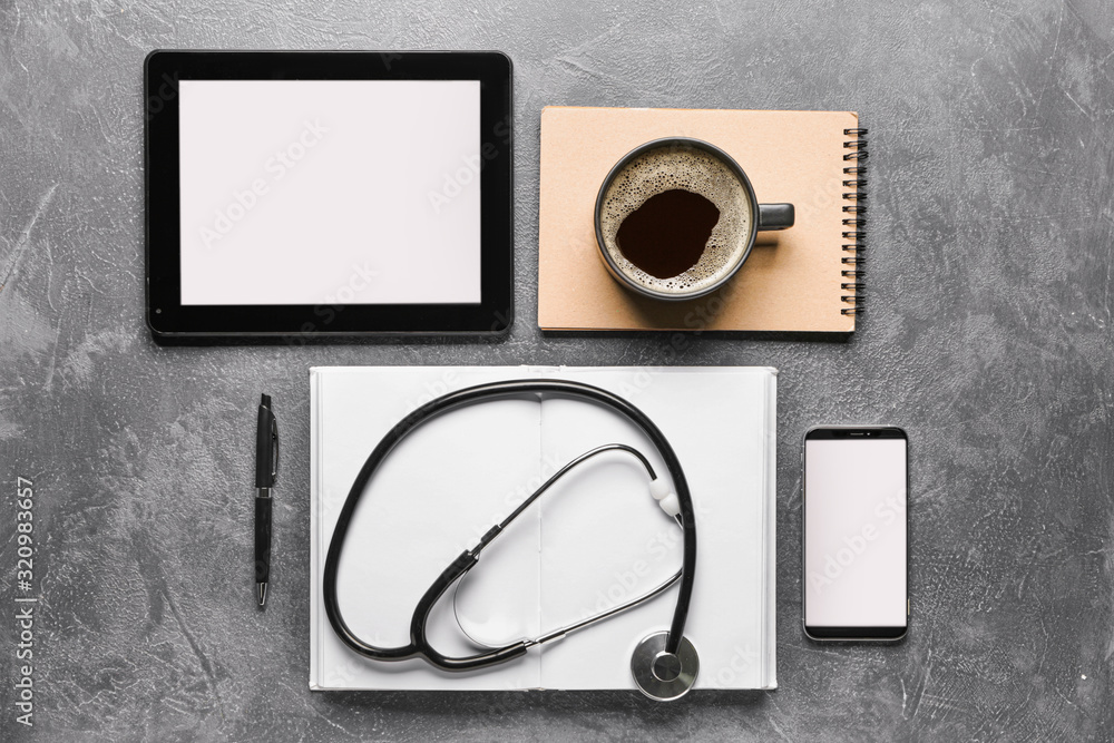 Stethoscope with tablet computer, mobile phone, notebooks and cup of coffee on dark background