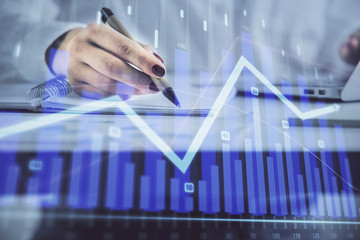 Double exposure of woman's hands making notes with forex graph hologram. Concept technical analysis.