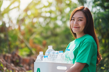 An asian woman collecting garbage and holding a recycle bin with plastic bottles in the outdoors