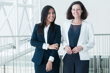 two happy business women posing at camera in office hall. colleagues looking at camera and standing 