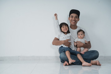 Wall Mural - two children who are happy sitting on his father's smiling lap when sitting on the floor with isolated background