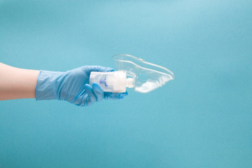 female hand in blue disposable medical glove holds nebulizer drug reservoir with silicone mask, inha