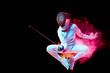 Pride. Teen girl in fencing costume with sword in hand isolated on black background, neon lighted smoke. Practicing and training in motion, action. Copyspace. Sport, youth, healthy lifestyle.