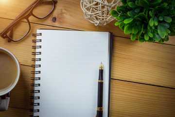 Blank notebook with pen and with glasses next to cup of coffee on wooden table,business concept.