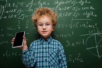 Wall Mural - smart child holding smartphone with blank screen near chalkboard with mathematical formulas