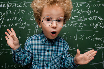 Wall Mural - surprised kid in glasses looking at camera near chalkboard with mathematical formulas