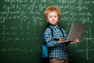 Wall Mural - curly kid holding laptop near chalkboard with mathematical formulas