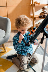 Wall Mural - smart child touching telescope while sitting on carpet