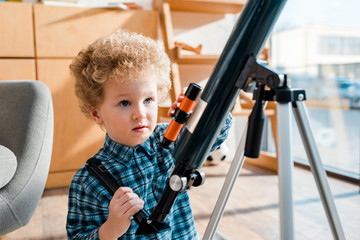 Wall Mural - smart and curly child looking at telescope