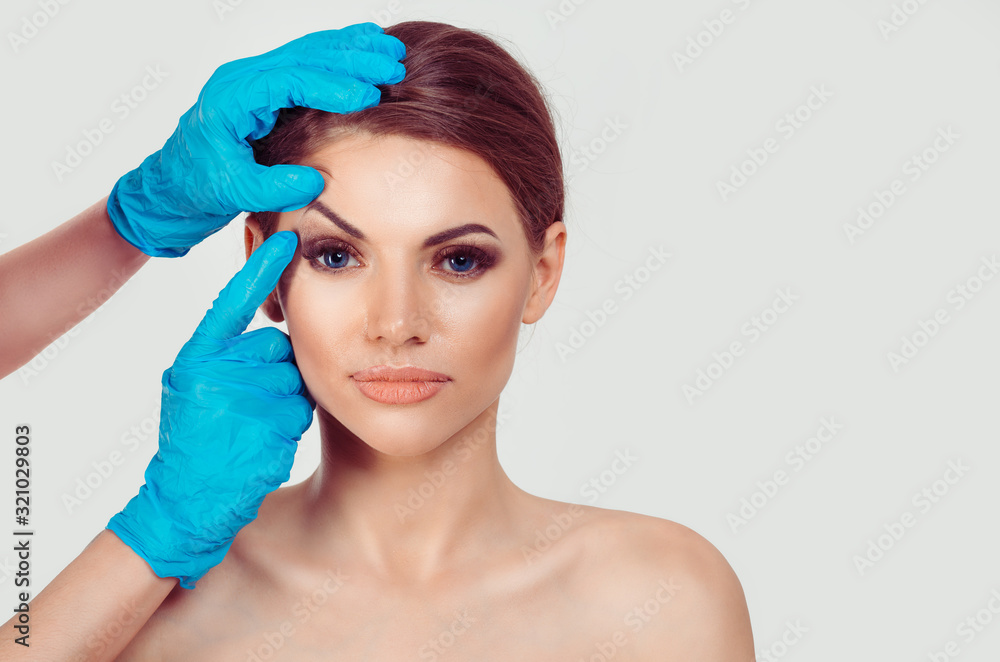 Upper eyelid blepharoplasty. Beautiful middle age woman getting ready for eyelid lift plastic surgery doctor hands in blue gloves point fingers to her eye on white. Beauty, people and health concept - obrazy, fototapety, plakaty 
