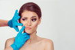 Preparing for cosmetic plastic surgery . Skeptical worried woman looks to the surgeon hands while the doctor examines her nasolabial wrinkle crease doubtful scared afraid, isolated white background