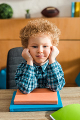 Wall Mural - smart child looking at camera near books on table