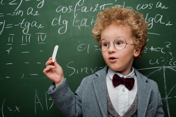Wall Mural - smart child in suit and bow tie holding chalk near chalkboard with mathematical formulas
