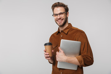 Portrait of cheerful young man posing with laptop and paper cup