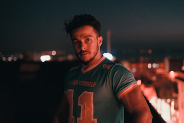 A strong brunette man with a blue gym shirt posing with the city light