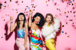 © LIGHTFIELD STUDIOS - excited multicultural girls having fun with glasses of champagne on pink with confetti