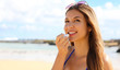 Smiling young woman applying sun protection on her lip on the beach. Attractive young woman putting lip balm on lips.