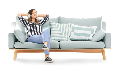 Young woman listening to music while sitting on sofa against white background