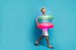 © deagreez - Full length profile photo of funky guy tourist walking seaside inside three colorful rubber lifebuoys swimmer wear striped sailor shirt cap shorts flip flops isolated blue color background