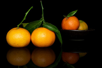 Wall Mural - Group of four whole fresh orange mandarin in glazed bowl isolated on black glass