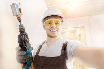 Builder worker man makes selfie photo with safety glasses and white helmet with pneumatic hammer drills