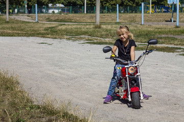 little girl child rides a children's red cool minimoto electric bike chopper motorcycle and poses in clothing style motorcyclists