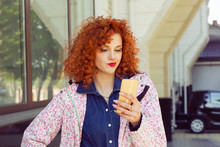 Skeptical Young Woman Reading E-mail On Her Mobile Phone, Standing In Street. One Single Person. Communication, Sms. Human Emotion Facial Expression Feeling, Reaction.