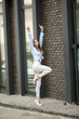 © ElenaBatkova - Stylish young woman in white jeans walks and bounces on city streets against brick wall.