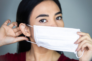 A woman putting on a medical disposable mask to avoid contagious viruses.