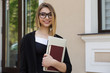 © hbrh - Student outdoor smiling. Closeup woman girl holding books laptop computer smile on face happy, black suit formal wear, eye glasses, bob hairstyle outside city urban home office on background