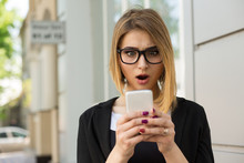 Woman Shocked With Sms Message On Phone. Closeup Woman Girl Looking At Cellphone Stunned Surprised Face, Black Suit Formal Wear, Eye Glasses, Bob Hairstyle Outside City Urban Home Office On Background