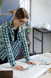 © YURII MASLAK - Architect drawing blueprints in office. Engineer sketching a construction project. Architectural plan. Close-up portrait of beautiful woman concentrated on work. Business construction concept.
