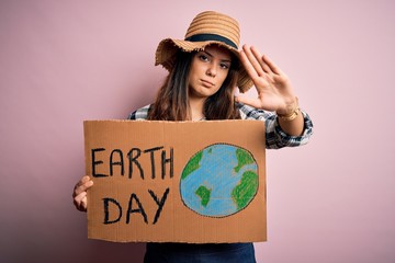 Wall Mural - Young beautiful woman asking for planet conservation holding cardboard celebrating earth day with open hand doing stop sign with serious and confident expression, defense gesture