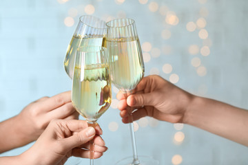 People clinking glasses of champagne against blurred lights, closeup