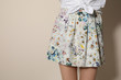 Young woman wearing floral print skirt on beige background, closeup