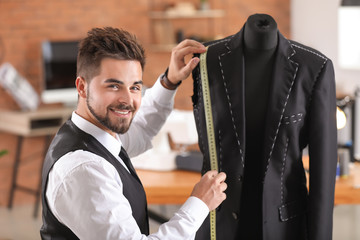 Wall Mural - Young tailor taking measurements of male jacket on mannequin in atelier