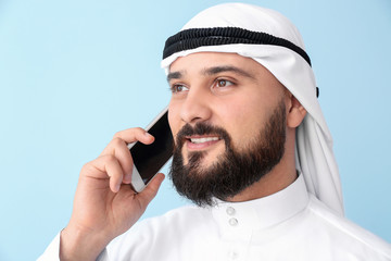 Wall Mural - Arab businessman talking by phone on color background