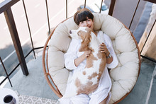 Overhead View Of Smiling Woman In White Clothes Relaxing In Round Soft Arm-chair With Beagle Dog. Portrait Of Cheerful Brunette Girl Having Fun On Terrace With Her Cute Pet.