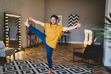Fototapete - Bright man standing on one leg practicing yoga at home