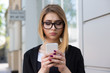 © hbrh - Upsetting message. Front view of a serious sad depressed girl checking a phone message walking on the street. Mixed race model in black business attire and glasses