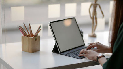 Cropped shot of female designer typing on blank screen tablet in simple co working space